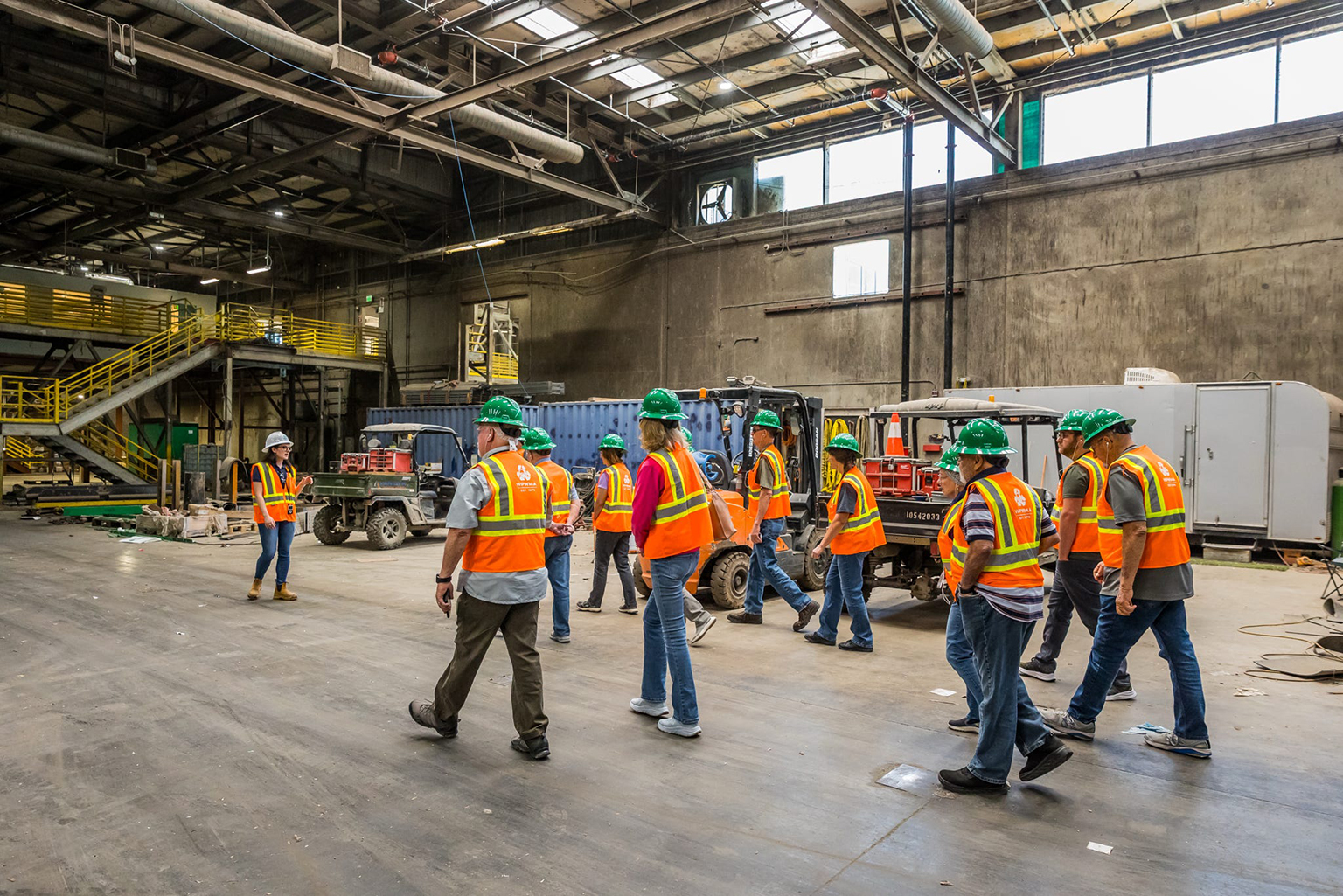 A group of visitors in safety vests and hard hats takes a tour of the Materials Recovery Facility of WPWMA