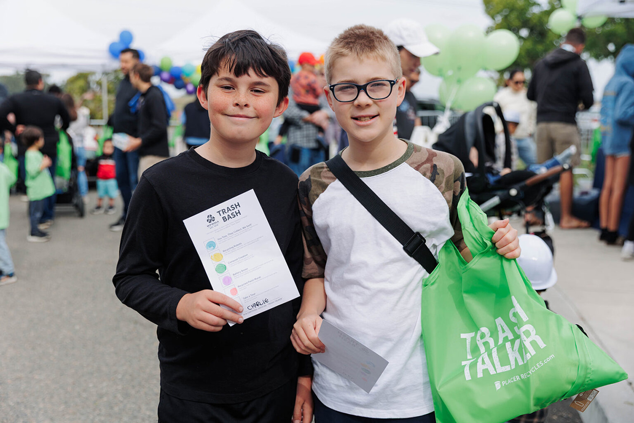 Two middle school boys smiling for the camera, holding a "Trash Talker" branded with Placer Recycles ecobag and holding a checklist for Trash Bash activities