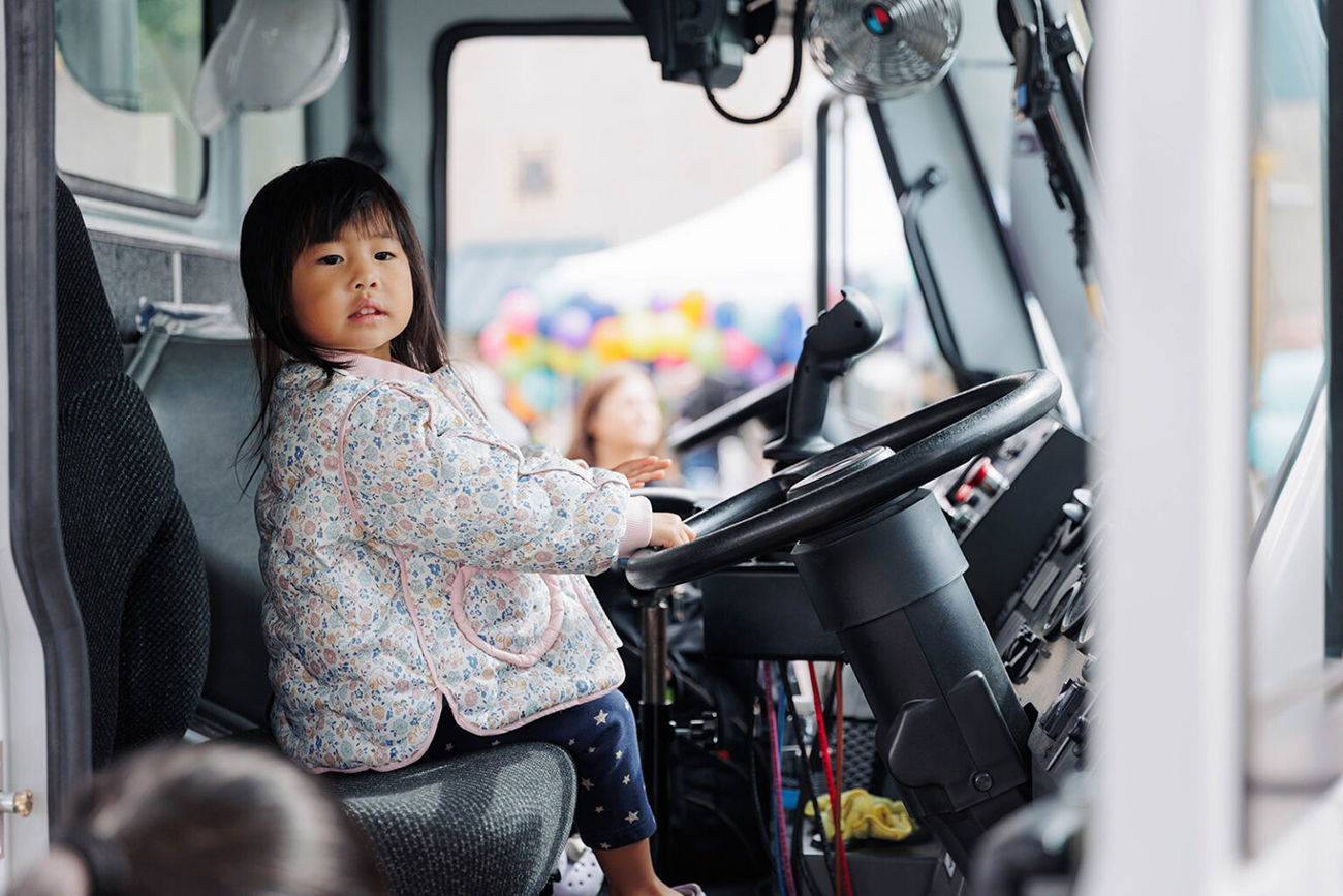 A young Asian girl sitting on a truck holding the steering wheel at the truck exploration activity of WPWMA's Trash Bash community event
