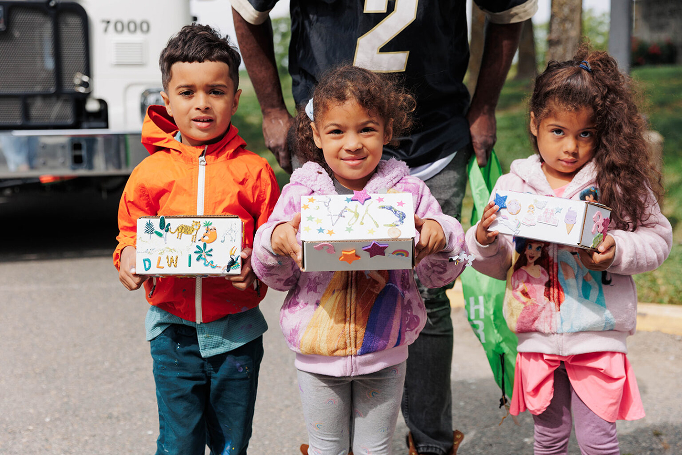 Outdoor shot of three children posing proudly with their hand decorated craft box