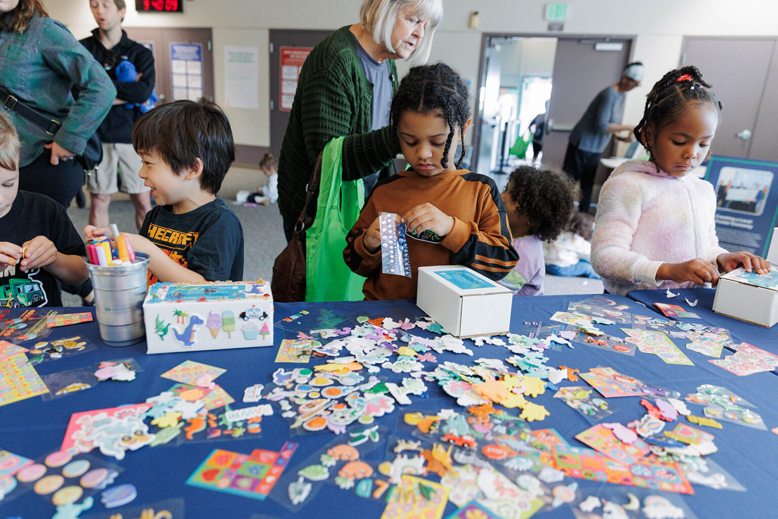 A group of children are engaging in hands-on crafting activities with various stickers and art supplies