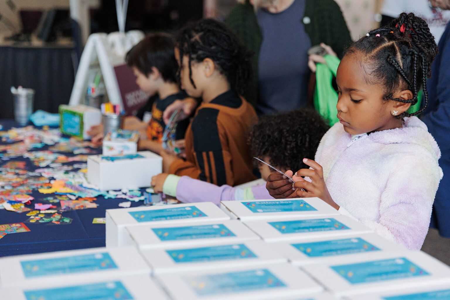 Children decorating boxes on a booth table with stacked boxes, stickers and various coloring and art materials