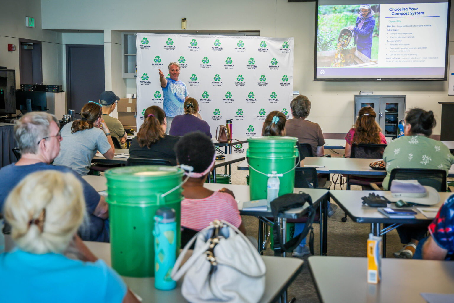 Man stands at front of classroom of attendees, presenting a PowerPoint on Choosing Your Compost System