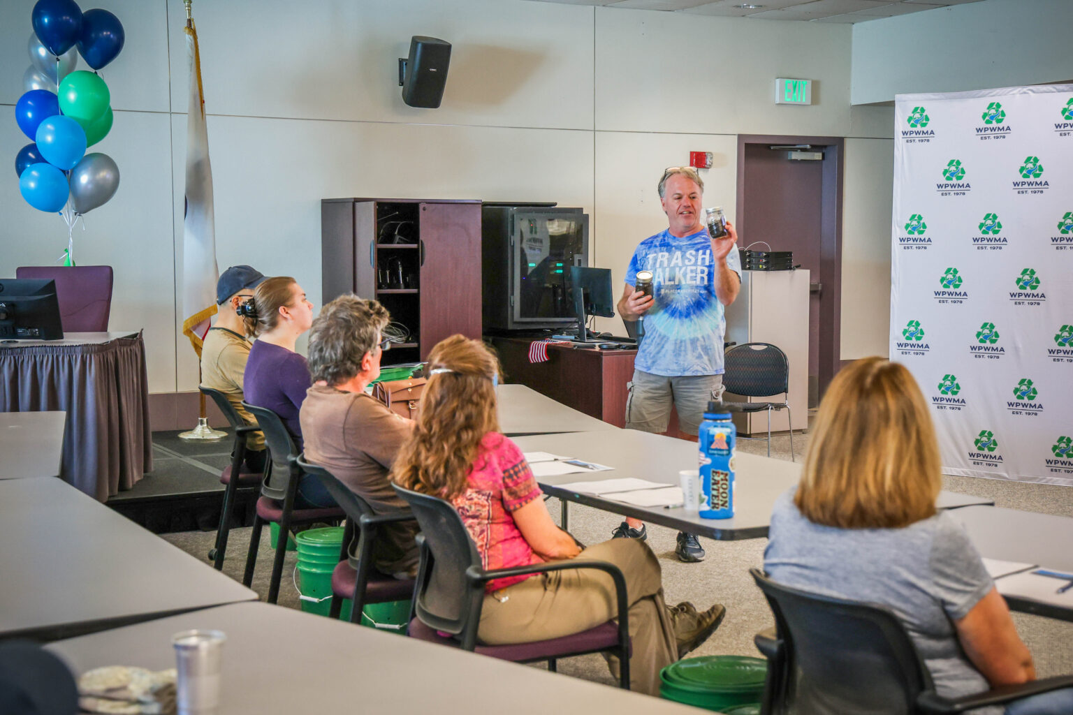 Man holds jars of compost and educates classroom of attendees about compost creation