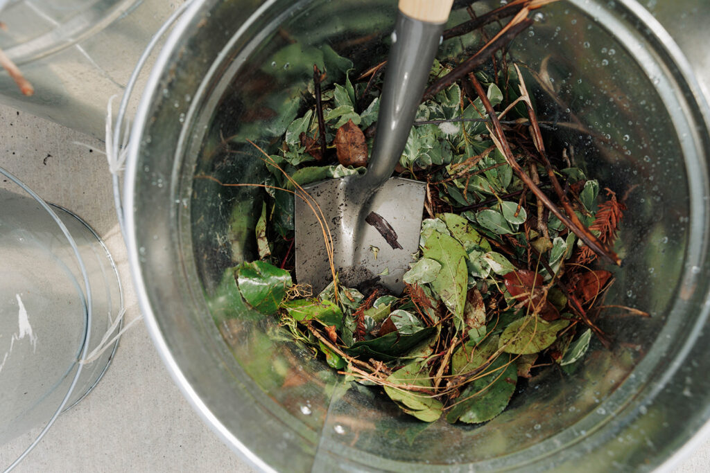 Metal bucket filled with green waste being stirred by shovel