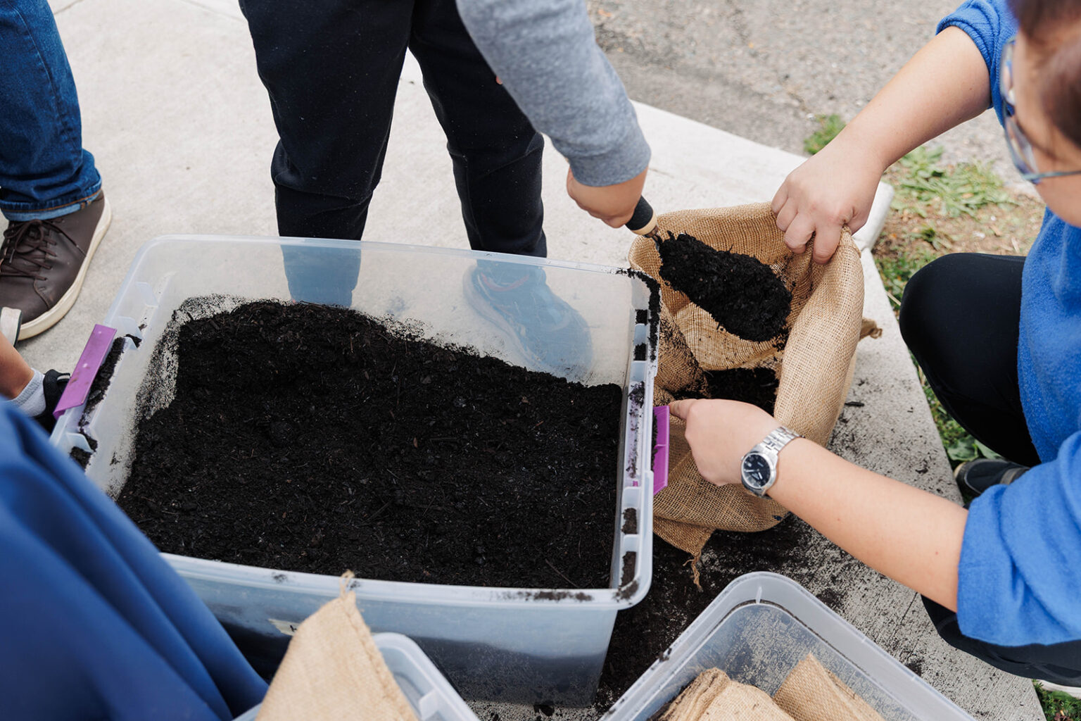 Group of people filling a burlap sack with compost soil from a large plastic container during the WPWMA Trash Bash event